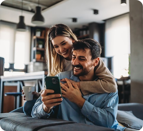 A smiling couple looking at a phone together on their sofa at home