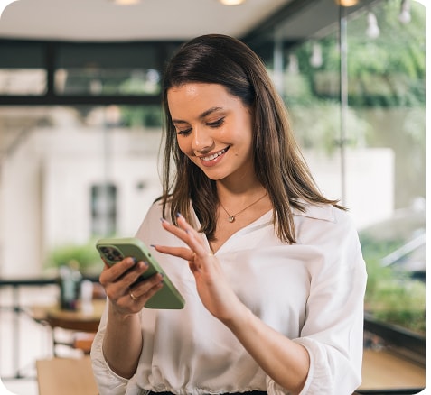A woman smiling while using her phone in a bright café